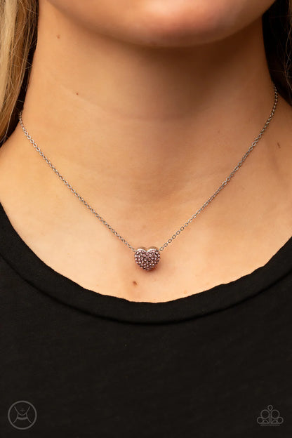 Necklace with a heart-shaped pendant worn by a person against a black background
