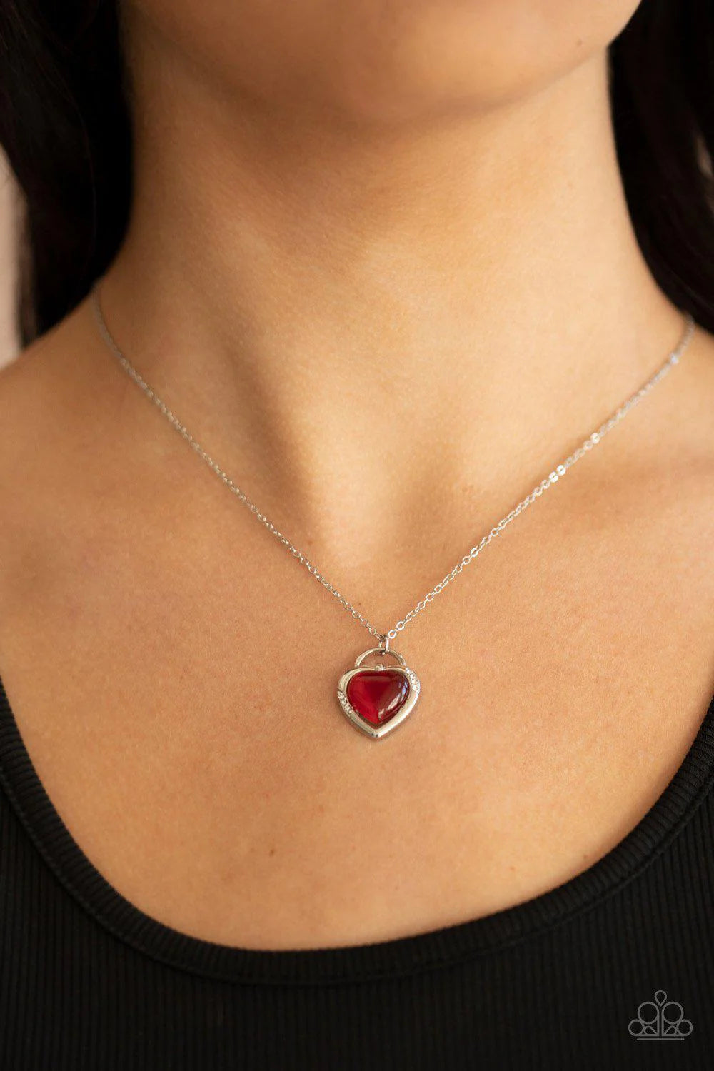 Silver necklace with a red heart pendant on a person wearing a black top.