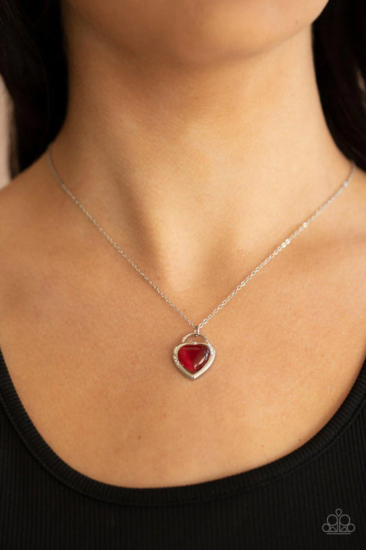 Silver necklace with a red heart pendant on a person wearing a black top.