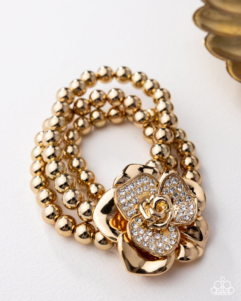 Gold beaded bracelet with a floral clasp on a white background
